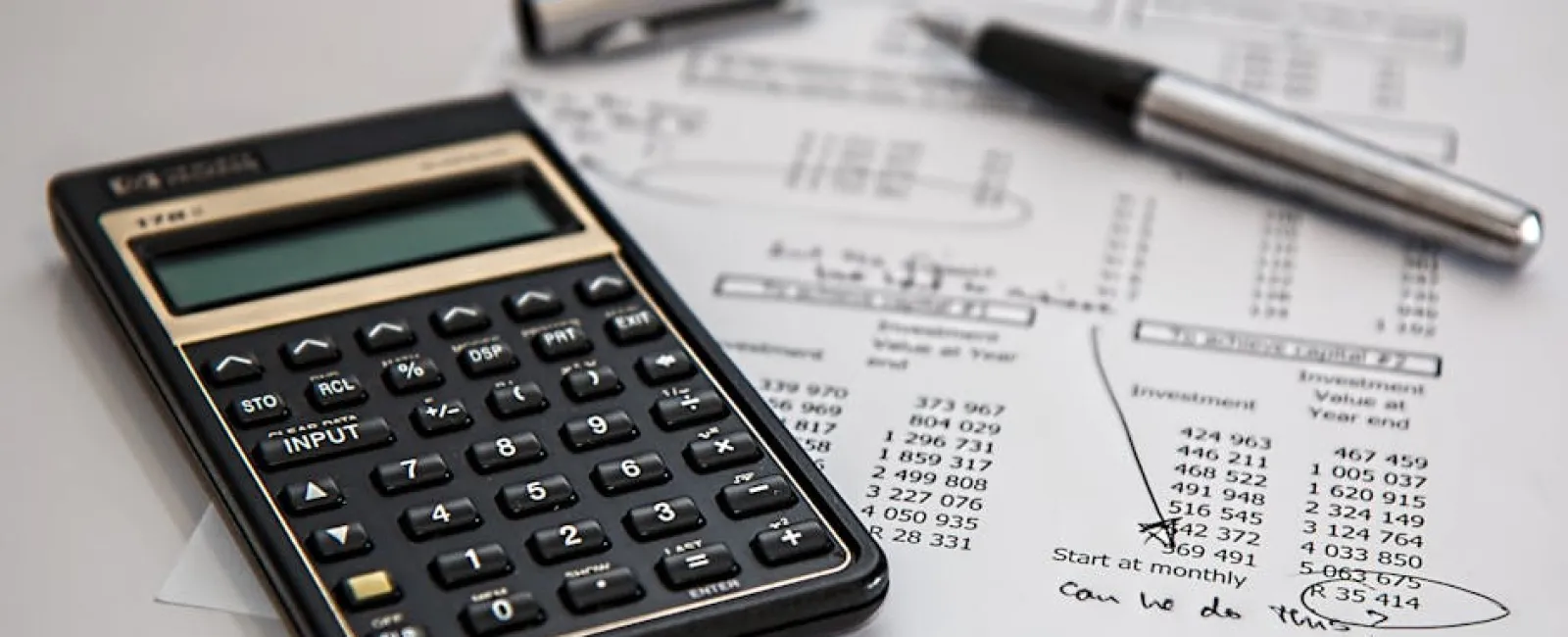 Black calculator on financial documents with a silver pen and handwritten notes about monthly investments.